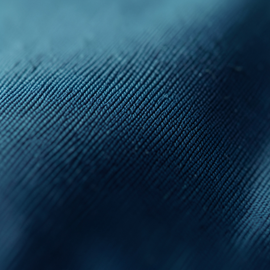 Extreme close-up photograph of smooth navy-blue fabric weave with fine diagonal threads catching faint light