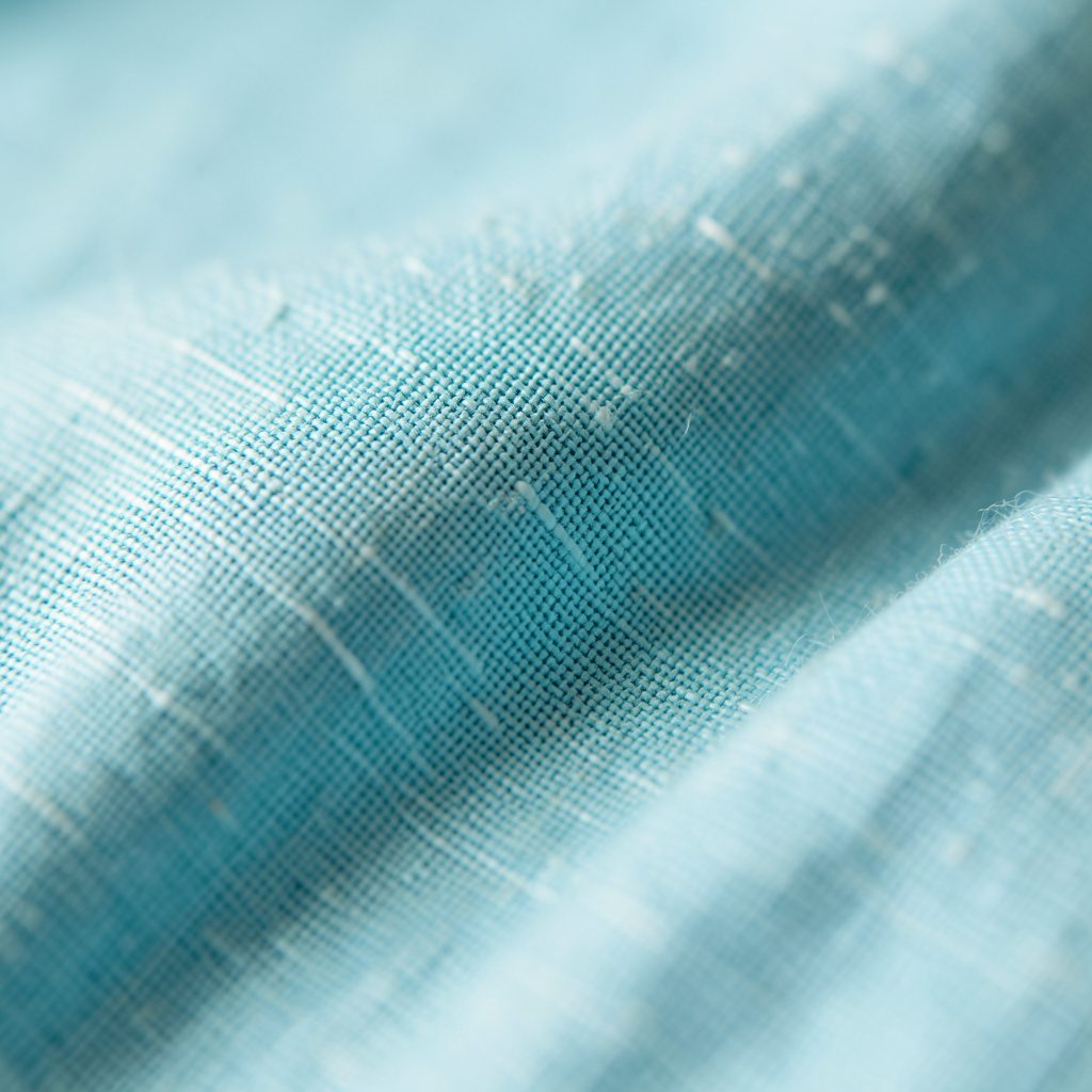 Extreme close-up photograph of textured linen fabric in soft sky-blue, with visible weave and gentle highlights